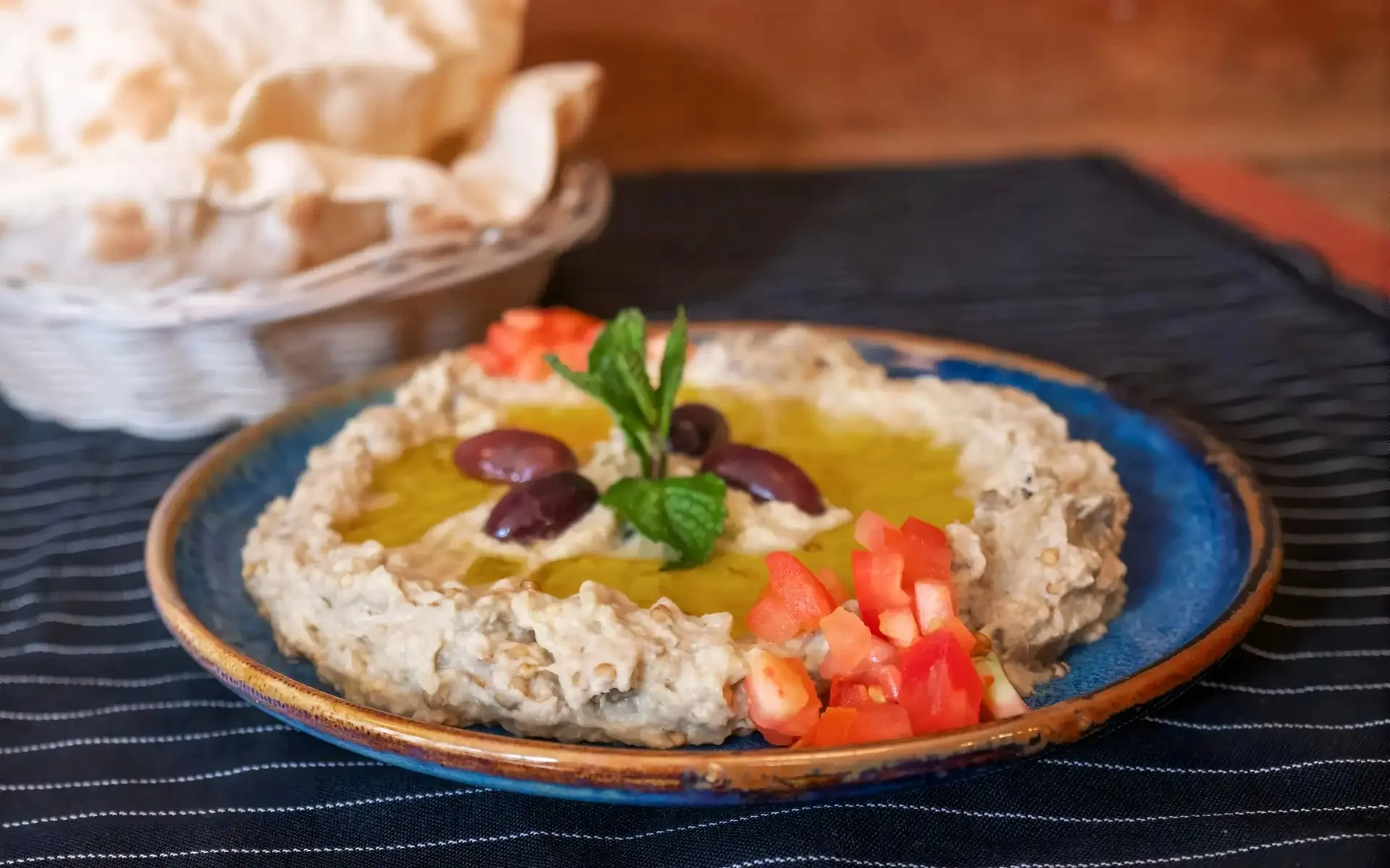 Plate of baba ghanoush garnished with olive oil, olives, and tomatoes.