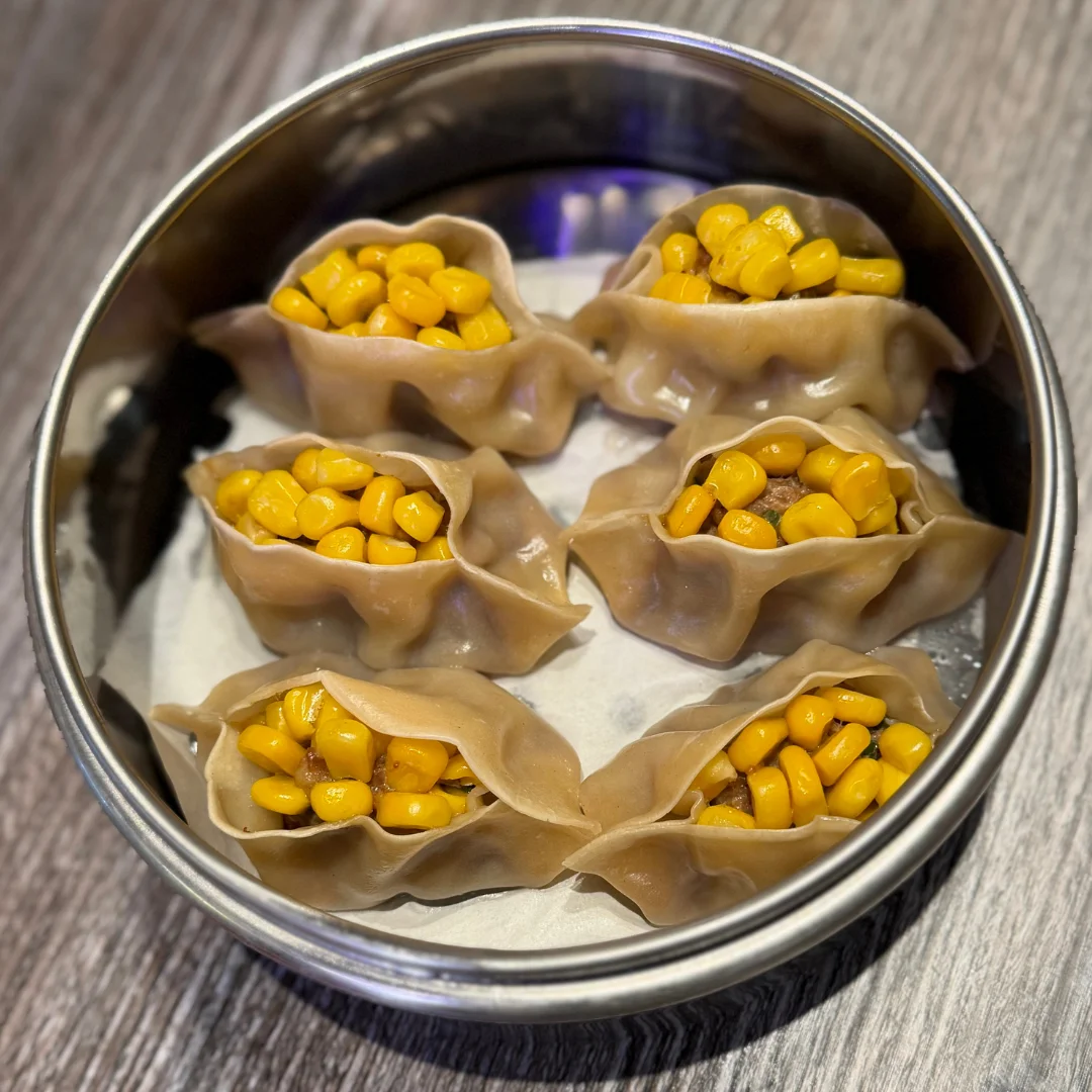 Steamed dumplings filled with corn in a metal steamer basket.