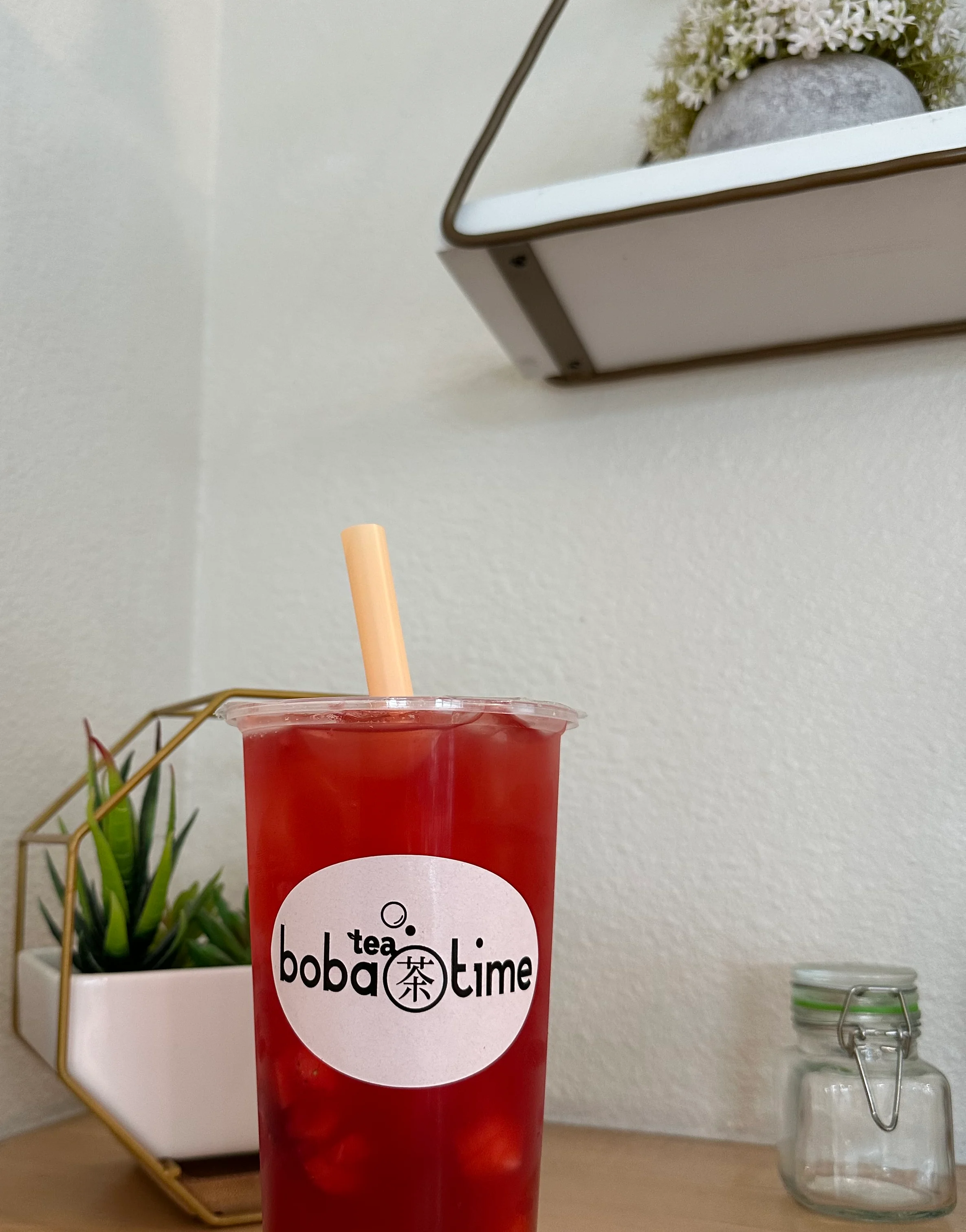 Two cups of colorful fruit-flavored drinks with bubbles at the bottom, set against a backdrop of drink dispensers and supplies.