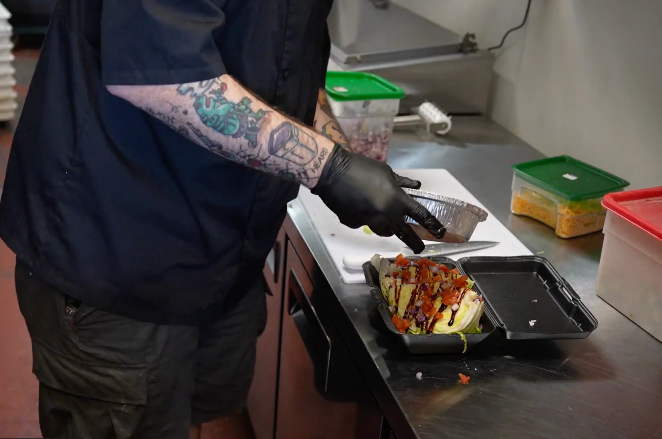 Restaurant worker preparing a loaded baked potato in a commercial kitchen