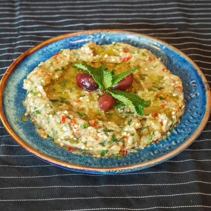 A plate of creamy dip garnished with olives and mint leaves.