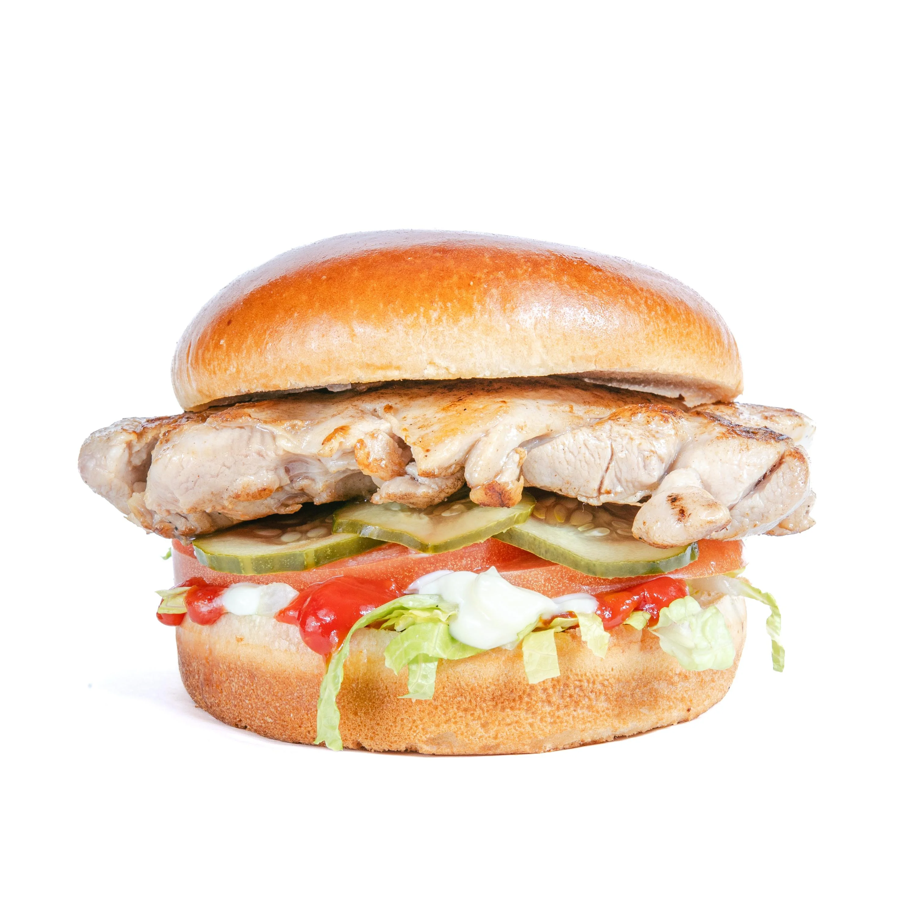 A grilled chicken burger with lettuce, tomato, pickles, and sauces, served in a toasted bun.