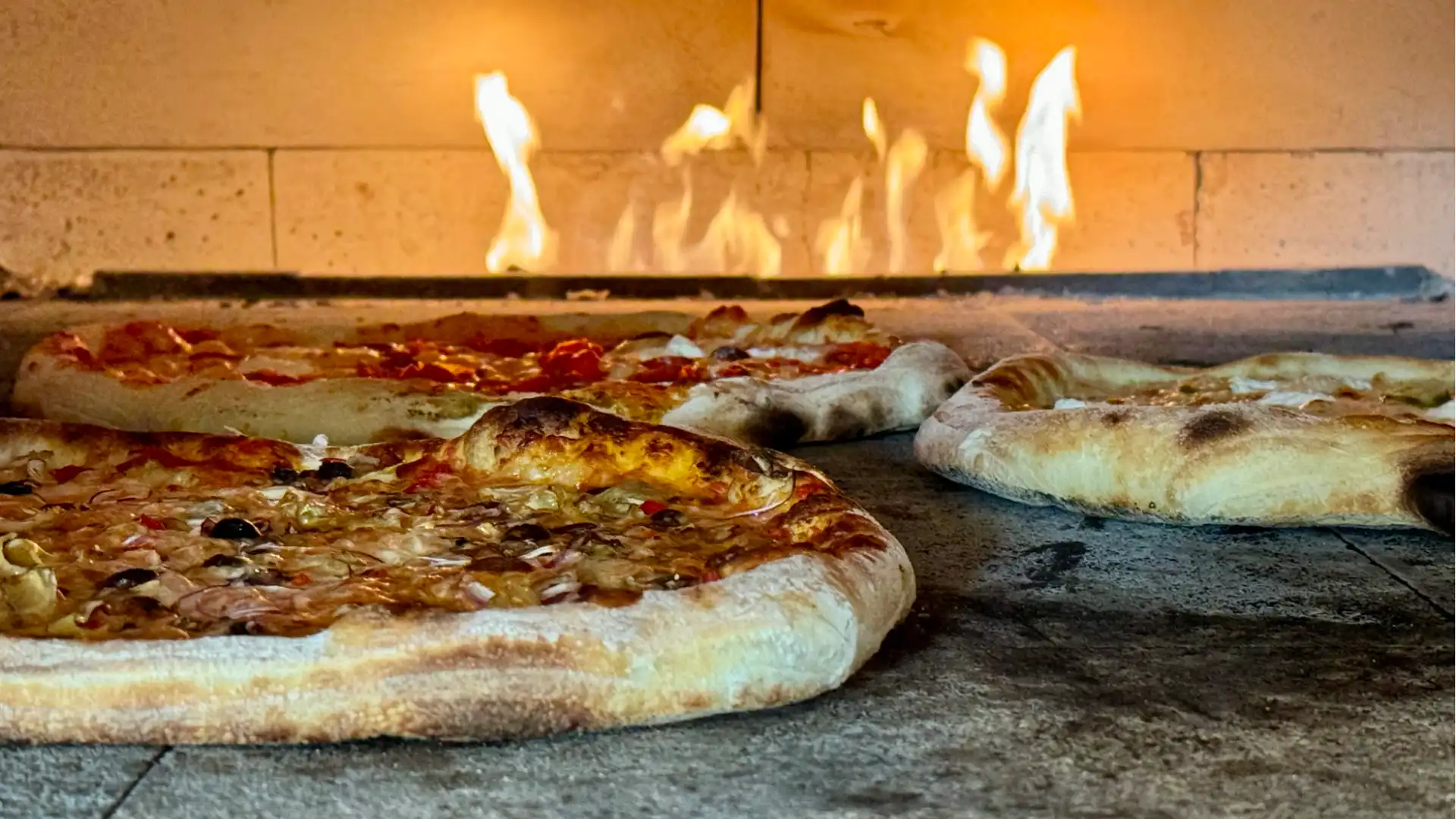 handcrafted pizza in a brick oven with flames in the background