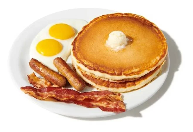 A hearty breakfast plate featuring fluffy pancakes, sunny-side-up eggs, sausage links, and crispy bacon.