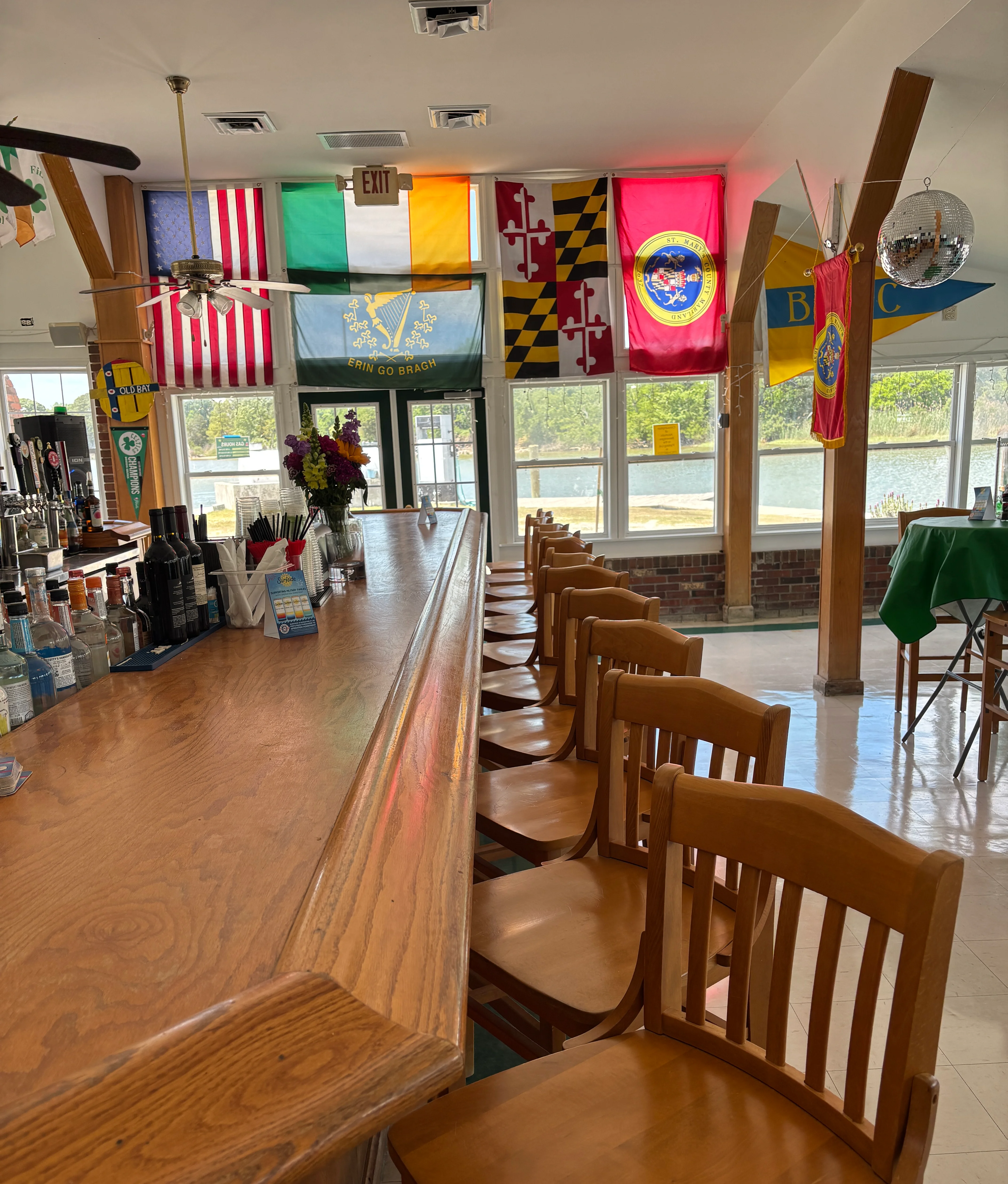 Interior of a bar with wooden chairs and various flags displayed.