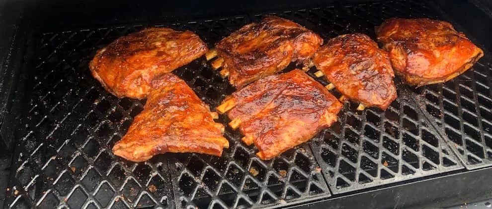 Racks of barbecue ribs cooking on a grill, coated in smoky sauce and charred to perfection.