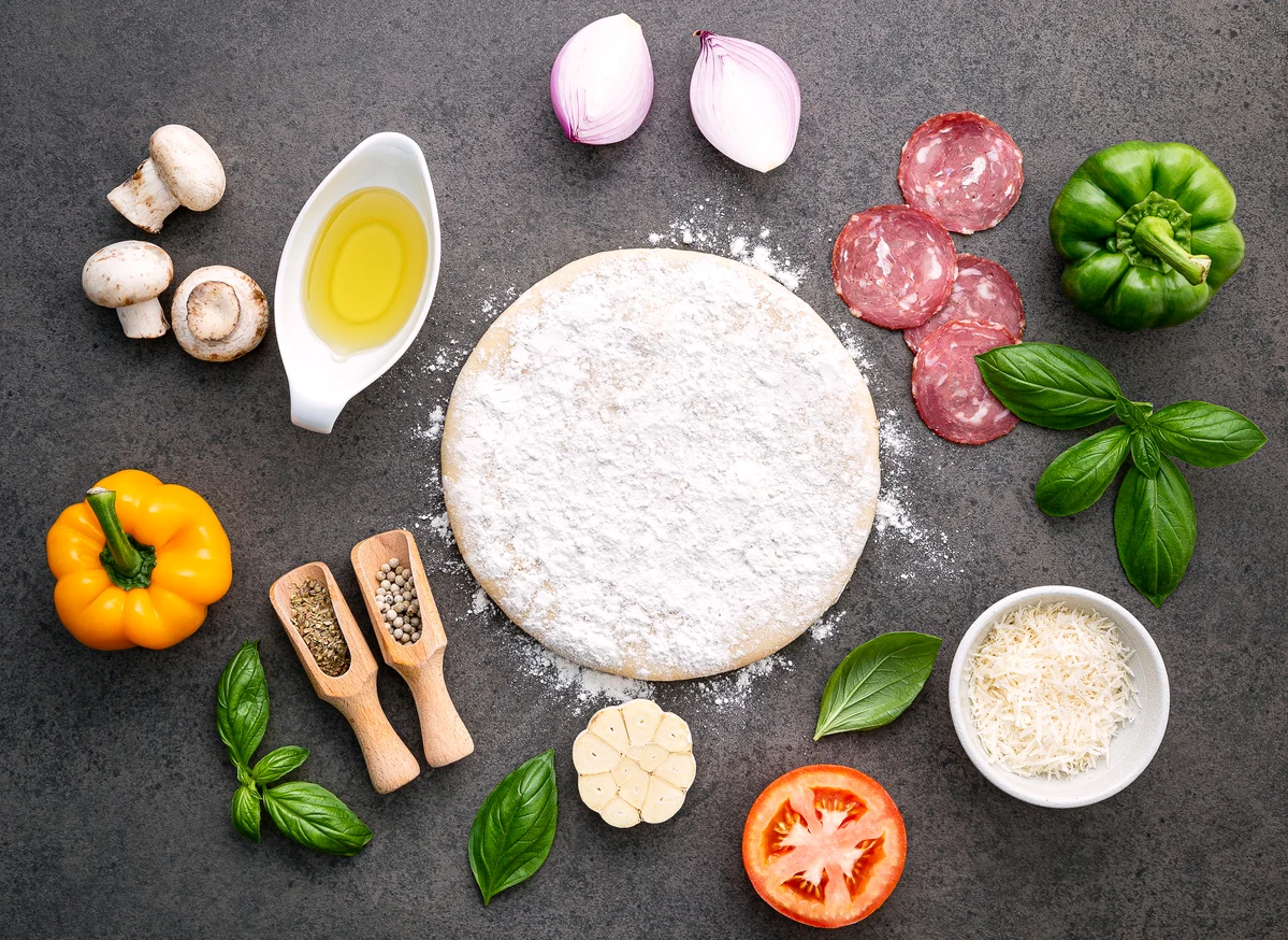 Ingredients for homemade pizza preparation on a dark countertop
