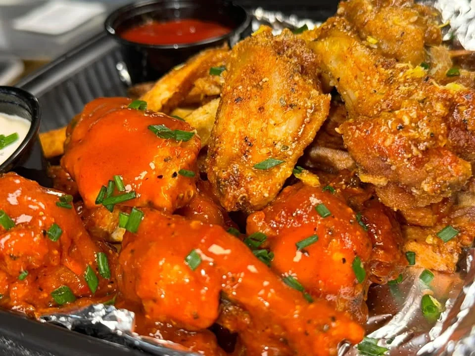 An appetizing platter of chicken wings coated in a spicy sauce, accompanied by a side of fries and dipping sauces. The wings are garnished with chopped herbs.