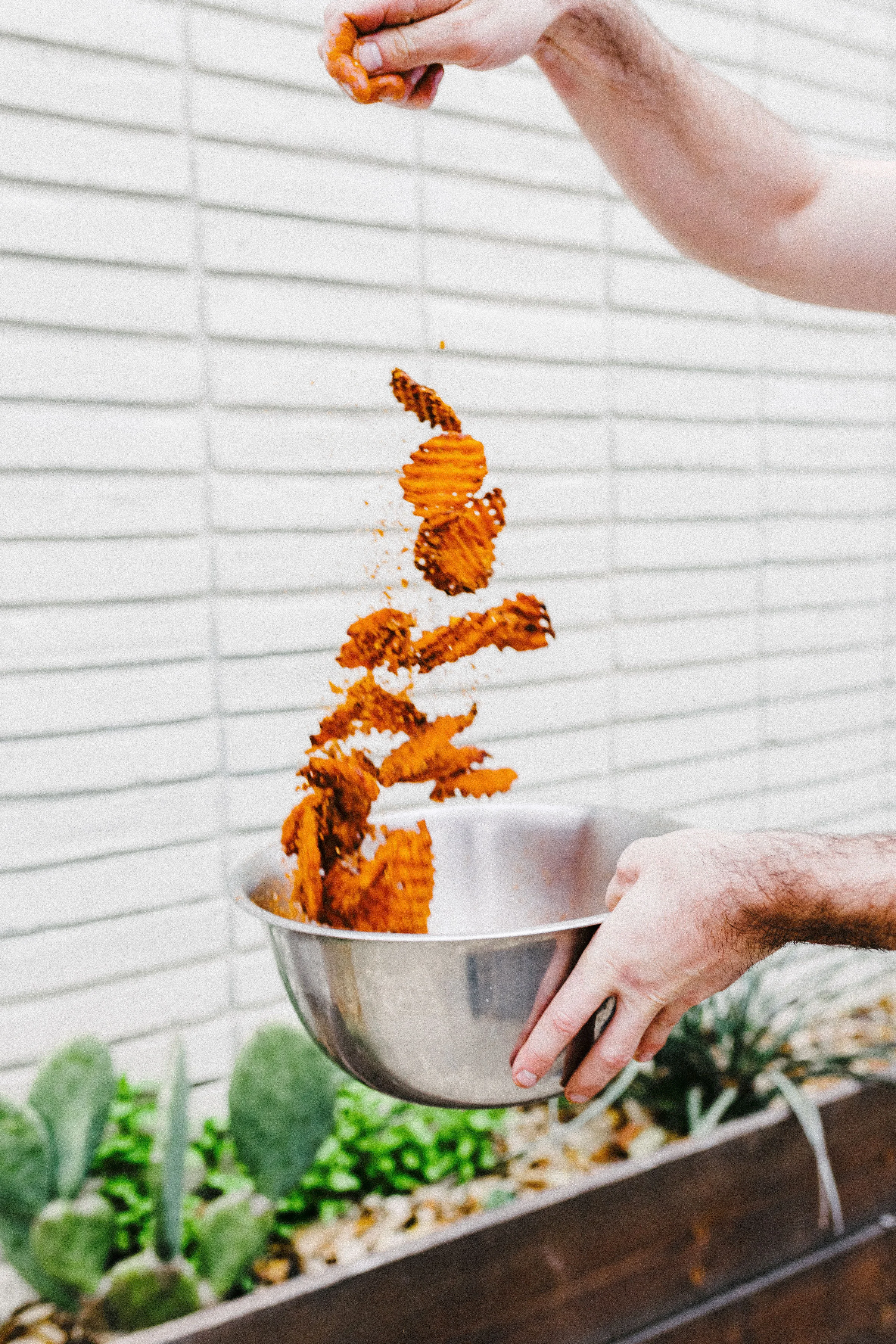 Crispy sweet potato fries being seasoned in a stainless steel bowl