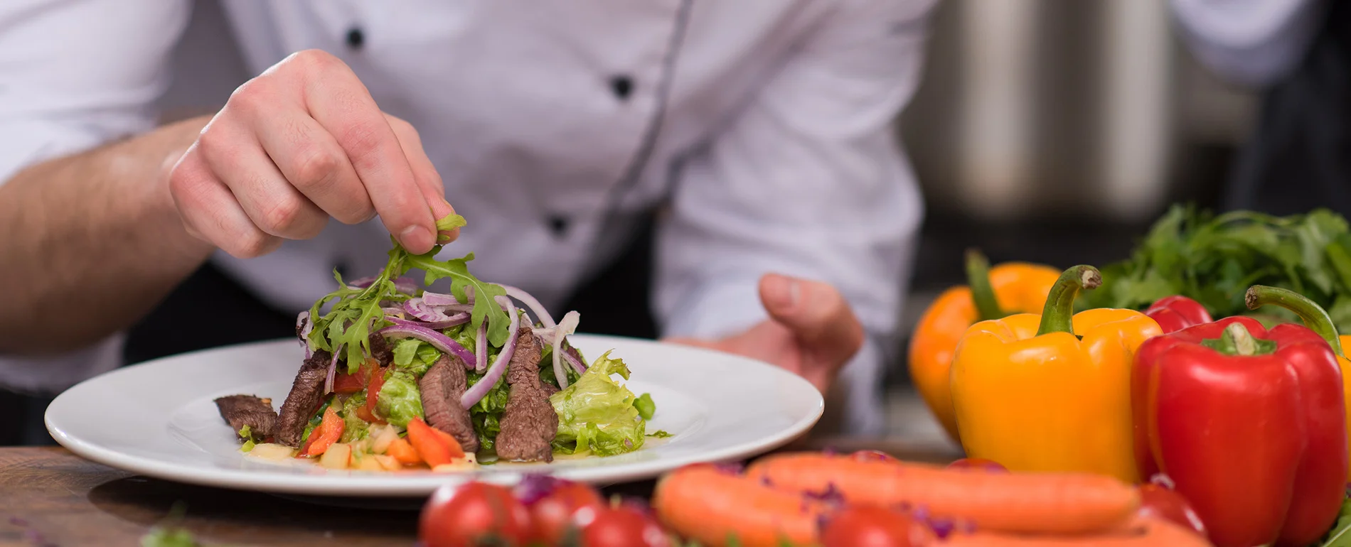 Chef plating a gourmet steak salad in a modern kitchen