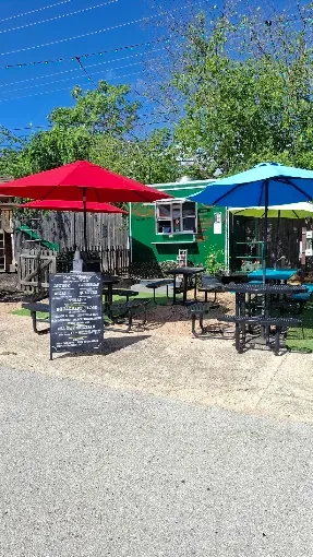 Colorful outdoor restaurant patio with umbrellas, picnic tables, and chalkboard menu