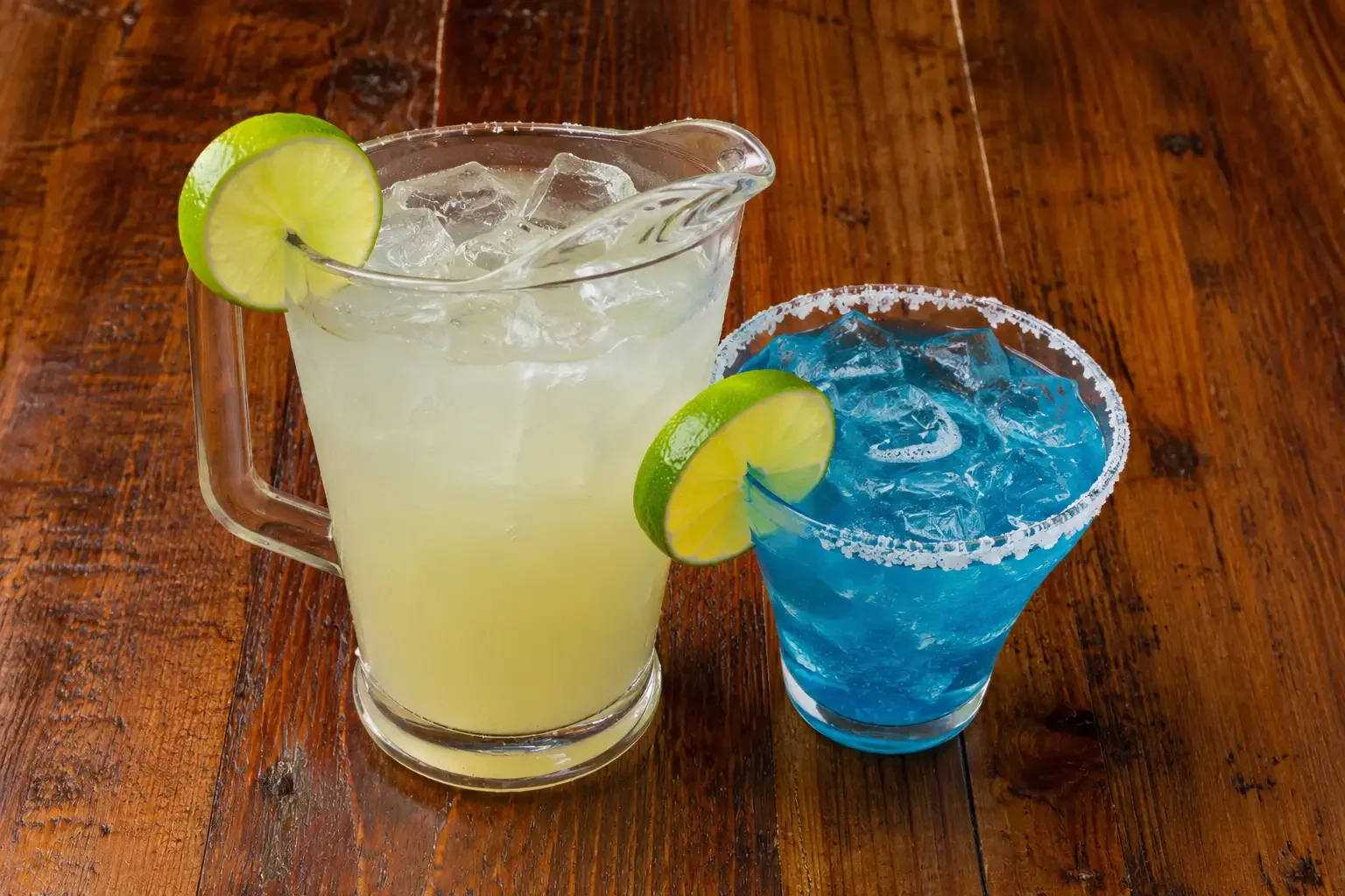 Colorful cocktails with lime garnishes in a pitcher and glass