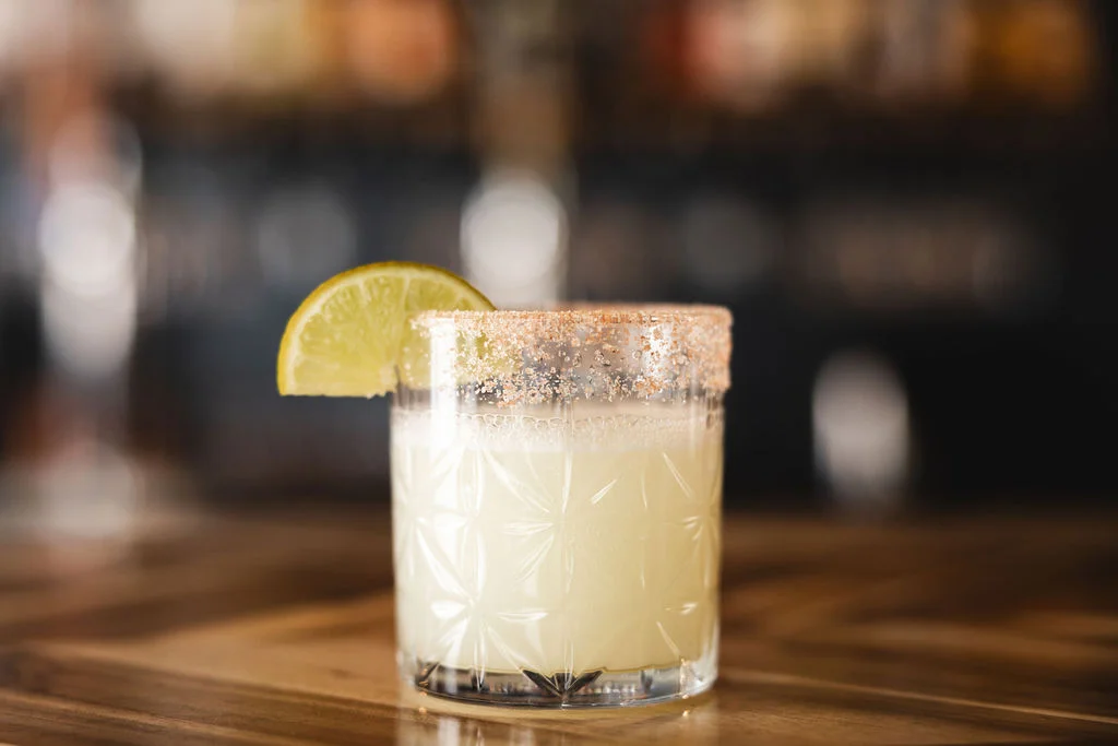 A refreshing cocktail served in a decorative glass with a lime wedge and a salted rim.
