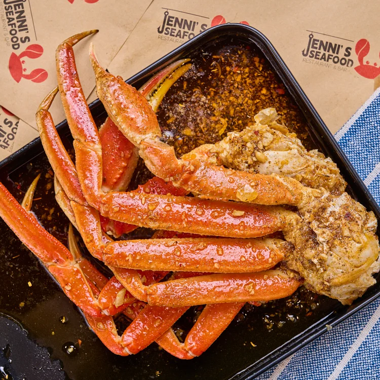 A close-up of a portion of seasoned crab legs served in a black container with a flavorful sauce.