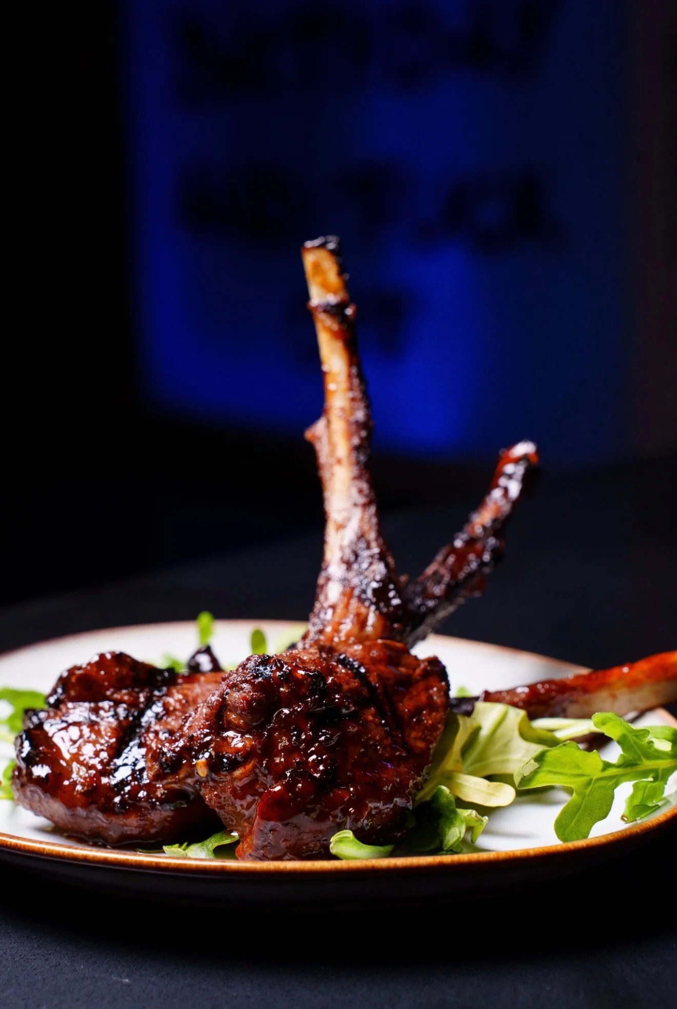 A beautifully plated dish of grilled lamb chops, garnished with greens and a dark sauce.