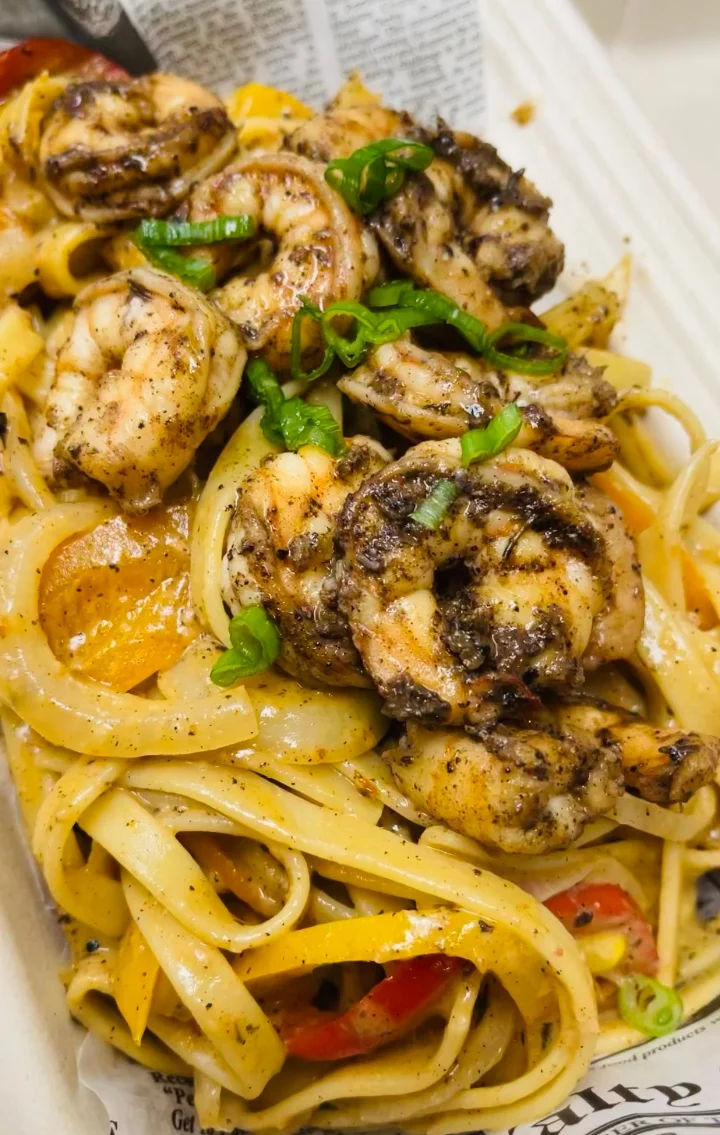 A delicious serving of fettuccine pasta topped with grilled shrimp and sprinkled with green onions, accompanied by assorted vegetables.
