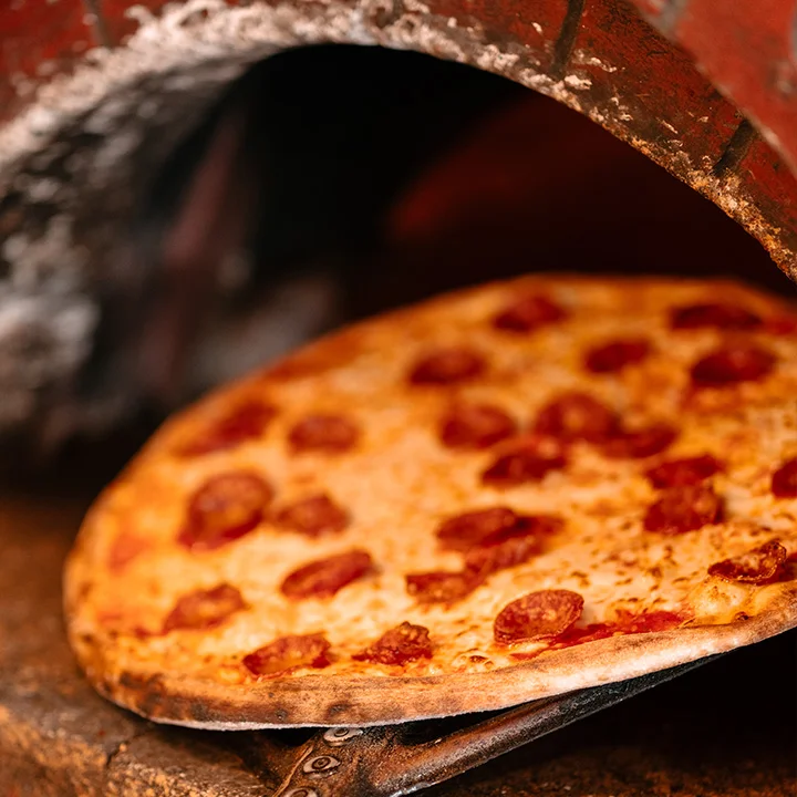 New York style pizza being pulled out of a wood-fire oven with a brick arch at the front