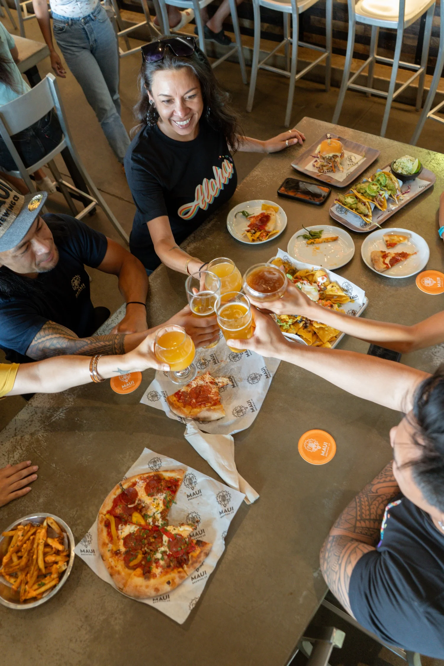 Group toasting with craft beers over pizza and nachos in a lively restaurant