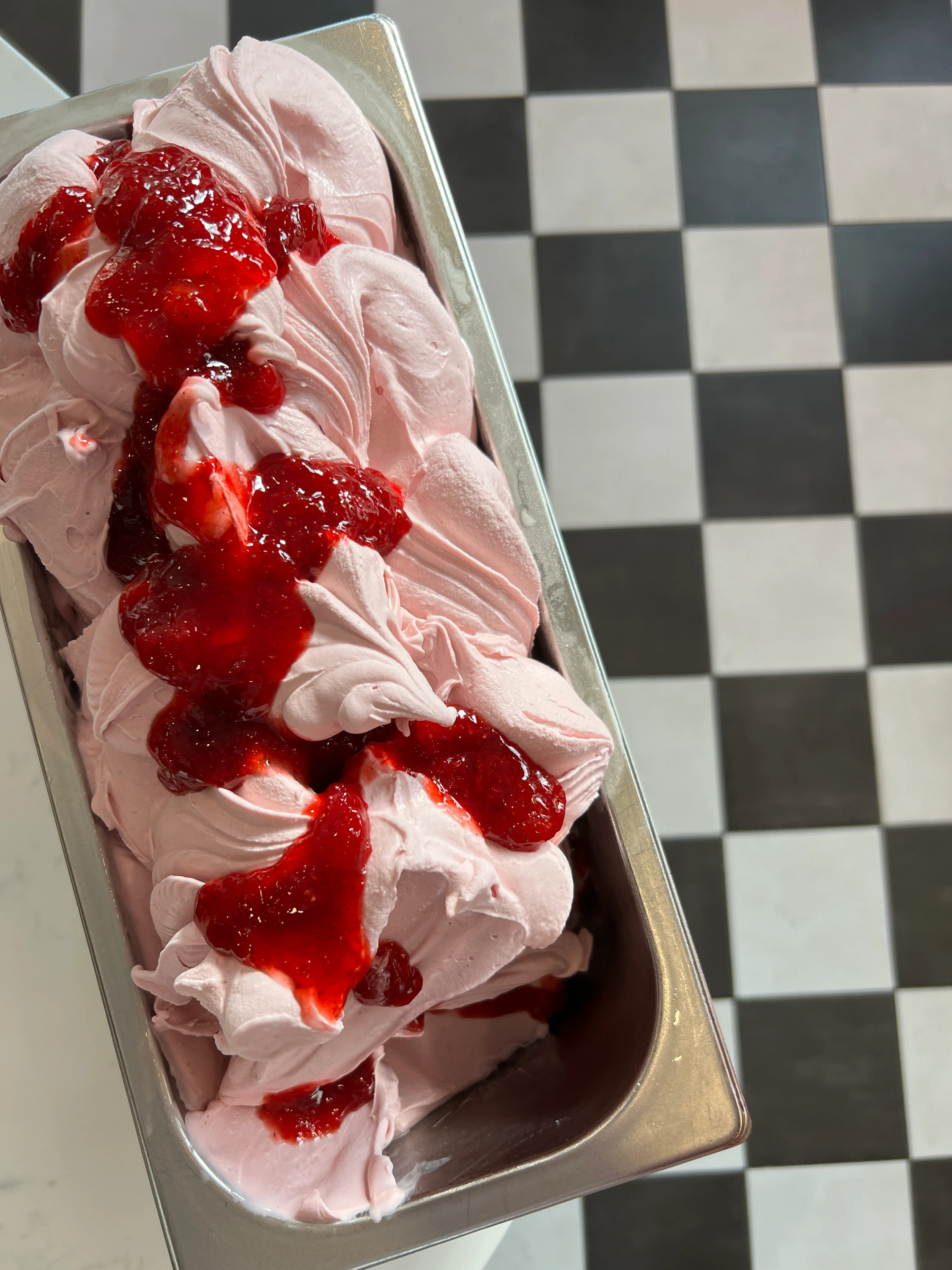 Strawberry gelato topped with berry sauce in a metal container