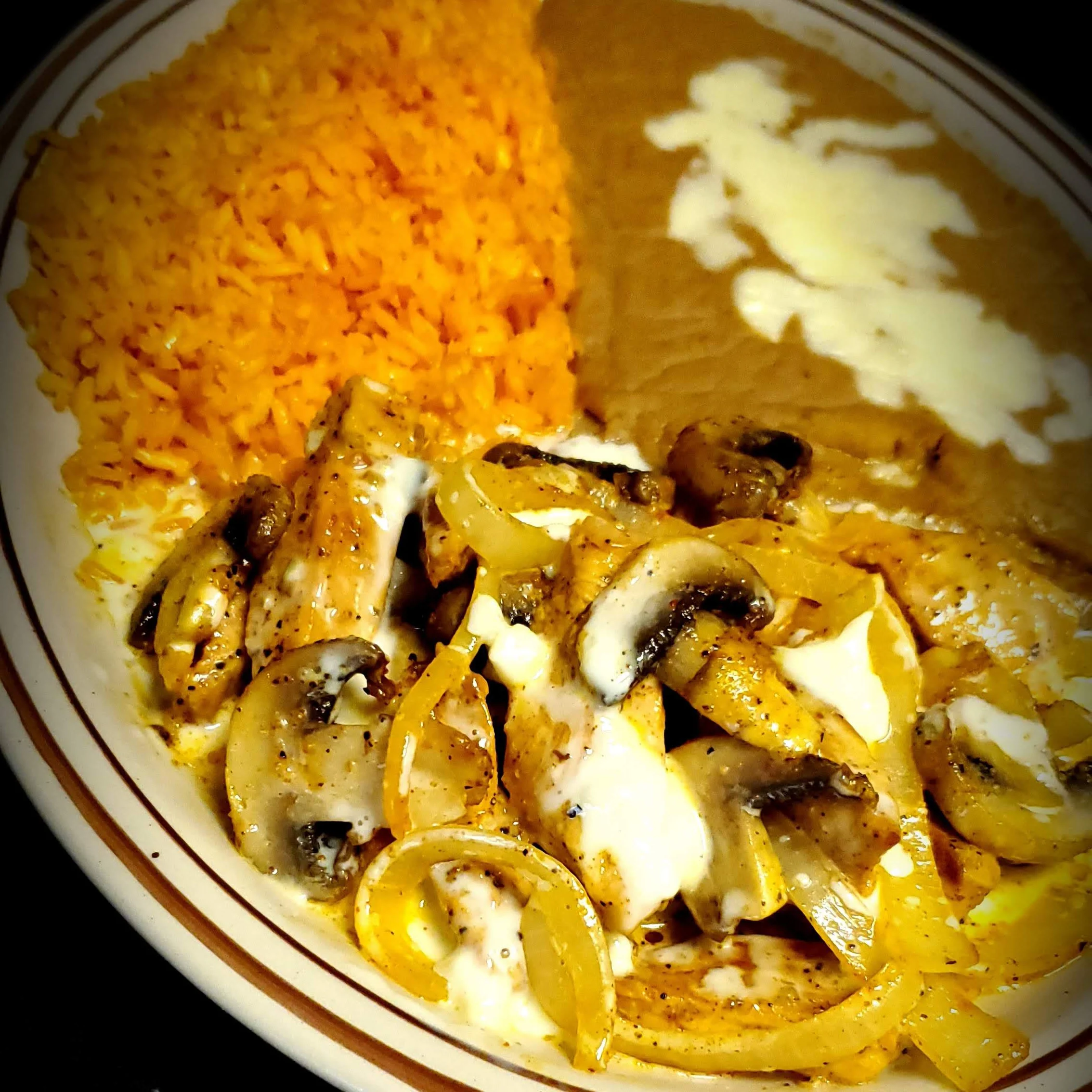 A plate of Texas Azada from El Charro Mexican Grill, featuring grilled chicken strips with sautéed onions and mushrooms, drizzled with queso dip, served with Mexican rice and refried beans.