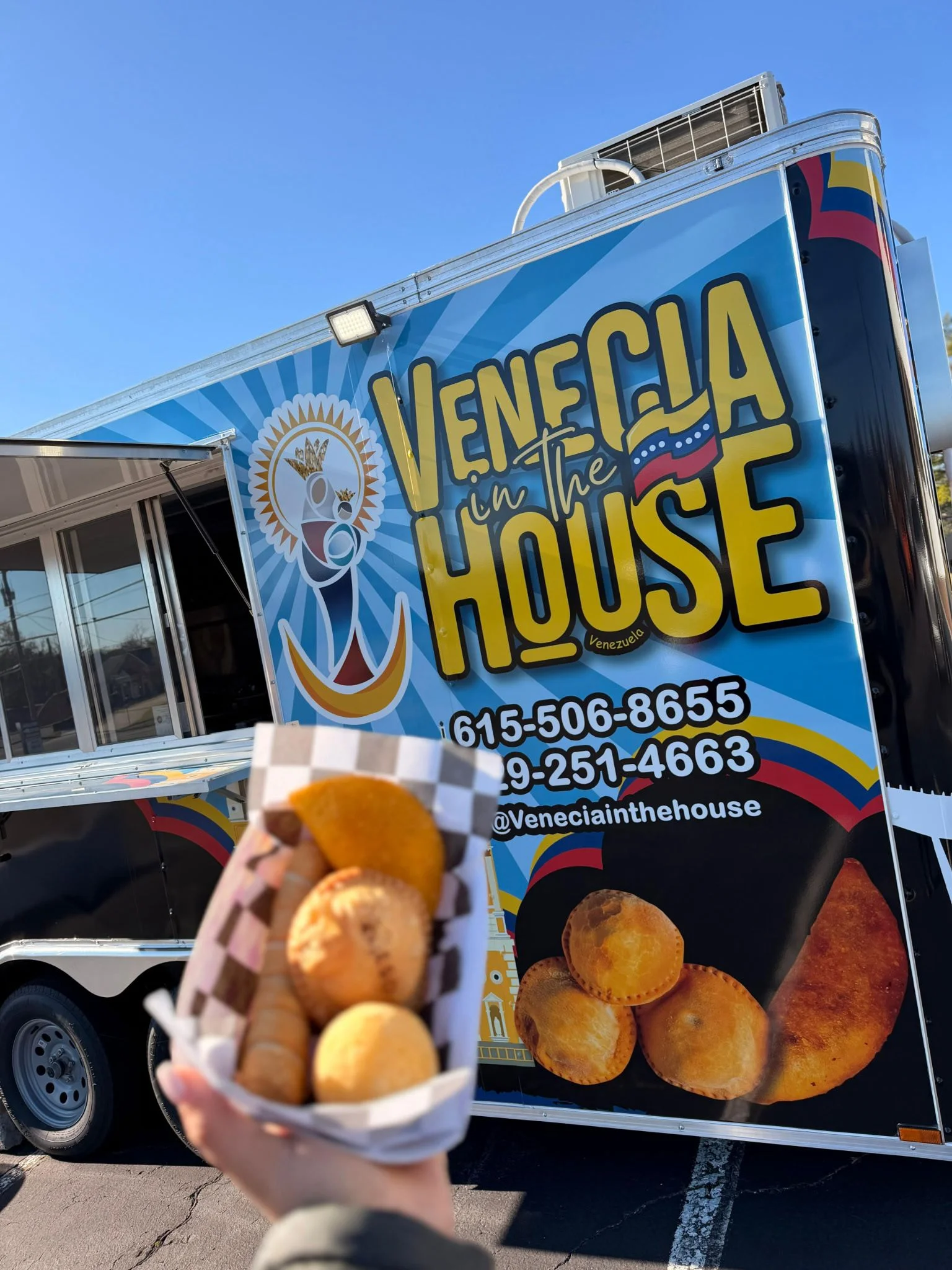 A close-up of a person smiling while holding a golden, crispy food item, wearing a shirt with 'Venecia in the House' printed on it.