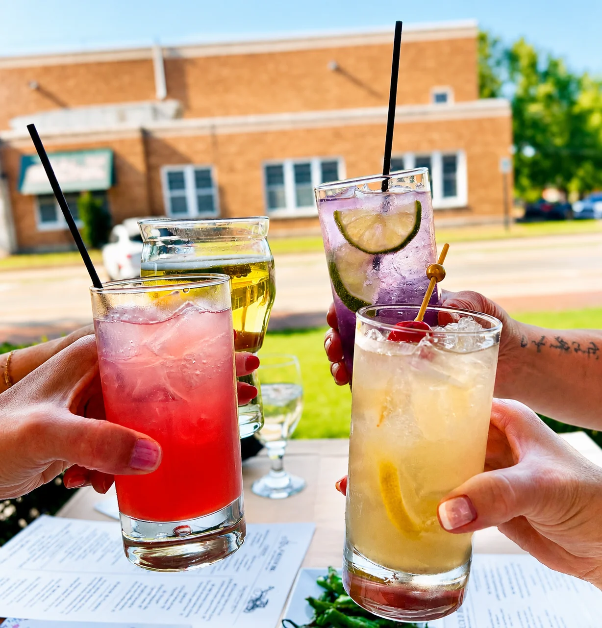 Colorful cocktails clinking together in a sunny outdoor setting