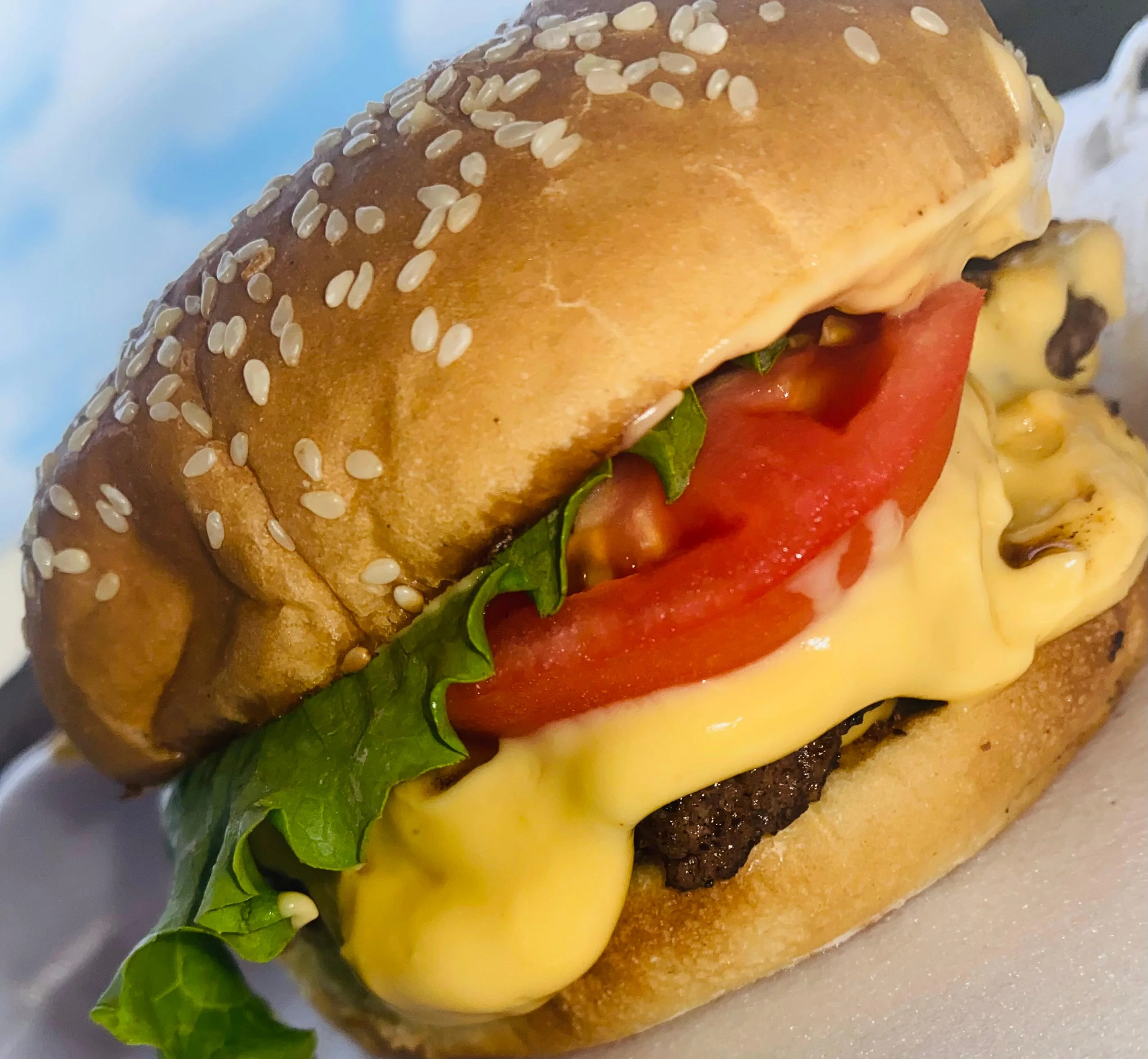 A cheeseburger featuring a grilled beef patty topped with melted cheese, lettuce, and tomato, all nestled in a sesame seed bun.