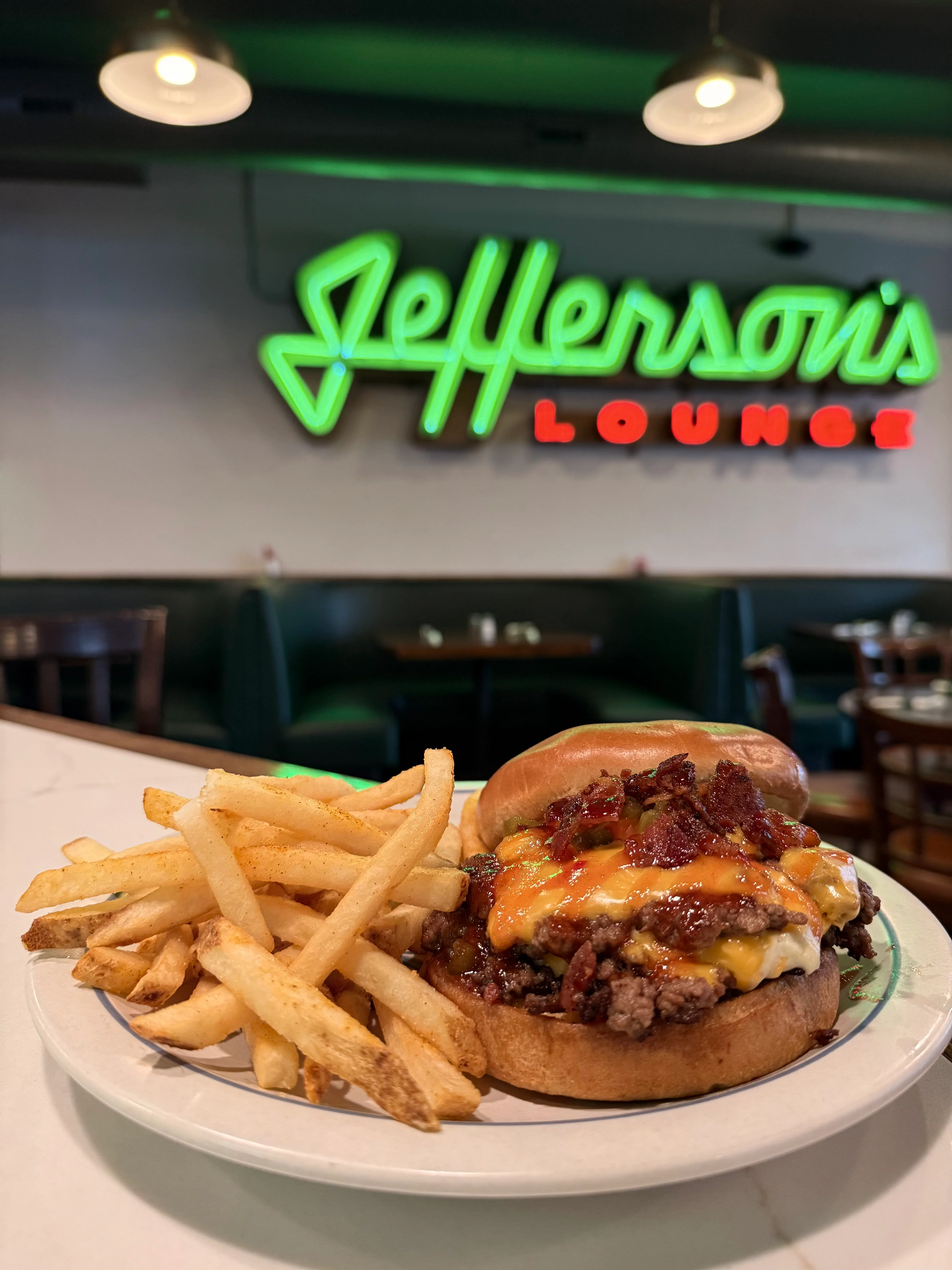 Juicy burger with fries in front of Jefferson's Lounge neon sign.