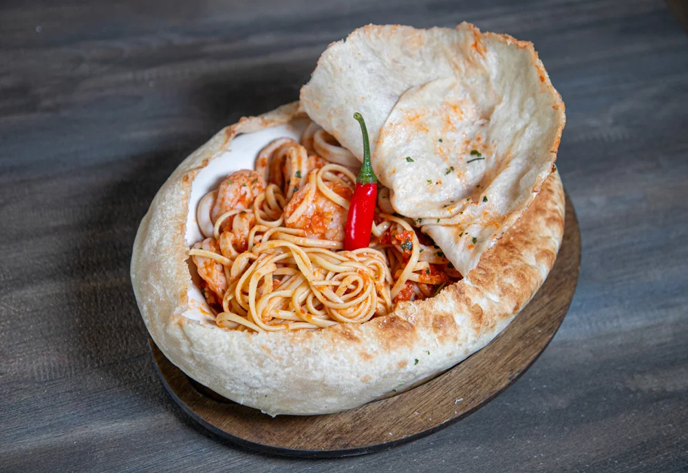 Spaghetti served in a bread bowl with chili garnish