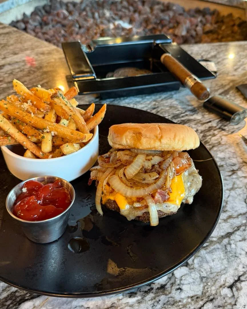 A classic cheeseburger topped with bacon and onions, served alongside seasoned fries and a small portion of ketchup.