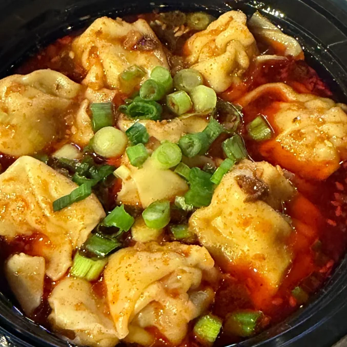 A bowl of dumplings in spicy sauce topped with green onions.