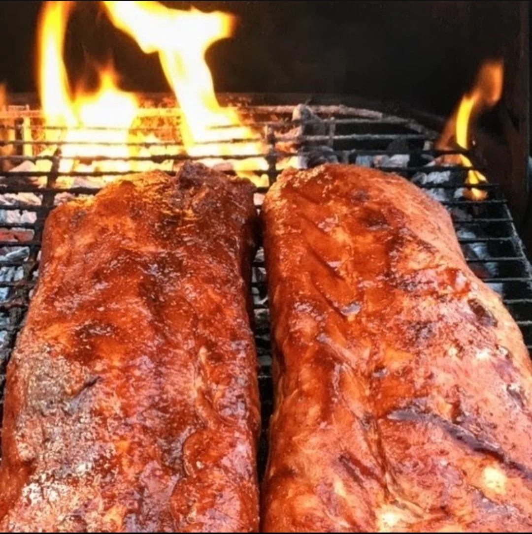 Juicy ribs grilling over an open flame, showcasing a rich color and marinated texture. The smoke adds flavor to the cooking process.