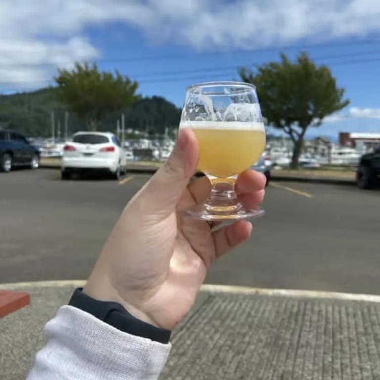 Hand holding a glass of craft beer with a marina view