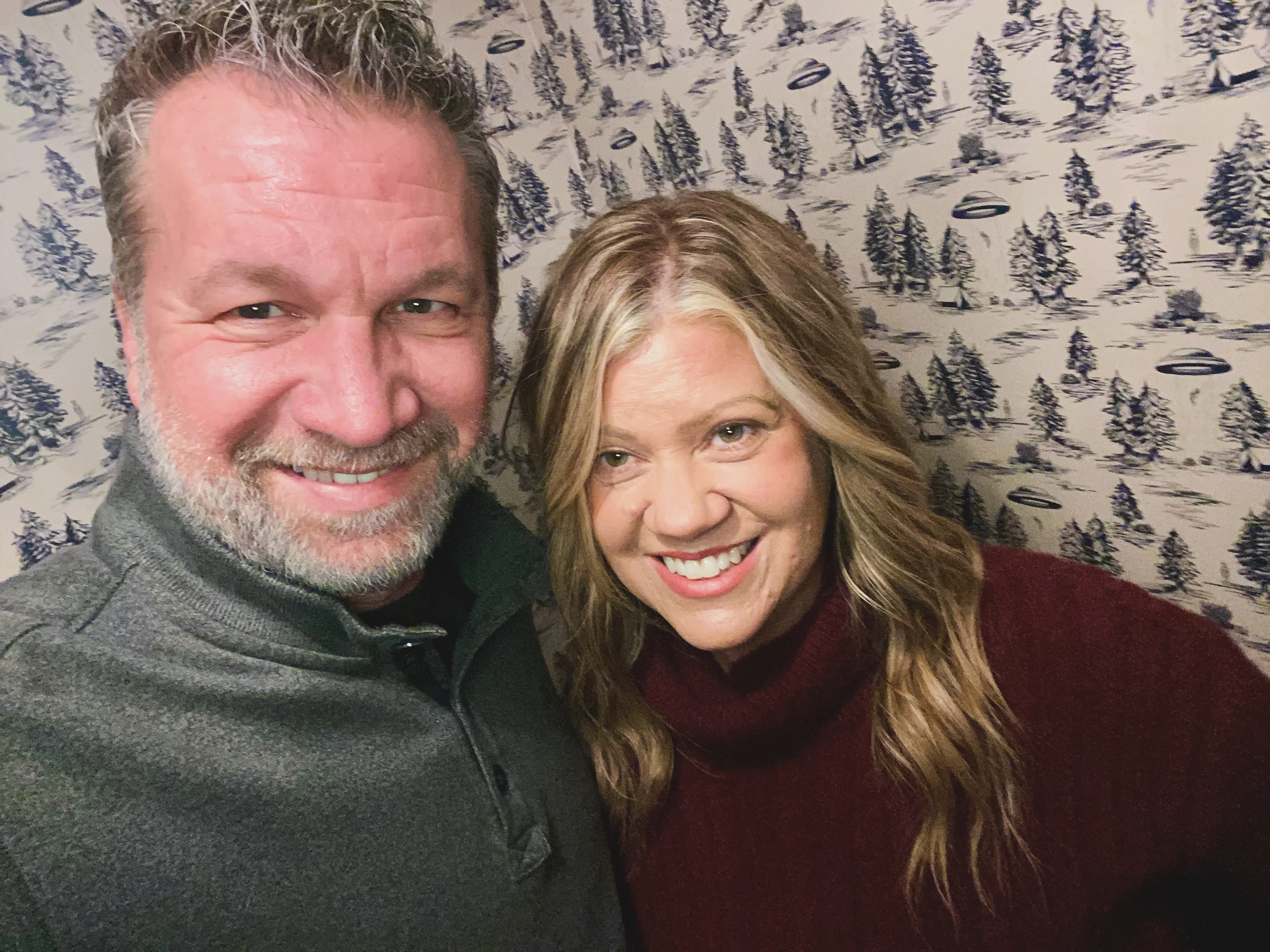 Happy couple smiling in a cozy setting with winter-themed wallpaper