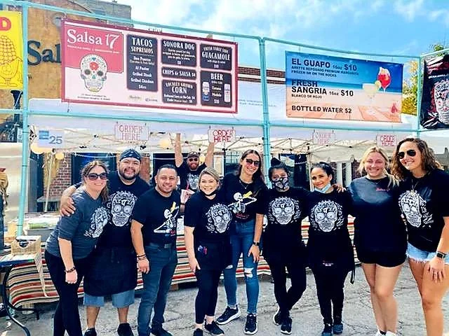 Team at a vibrant food festival booth serving Mexican tacos and drinks