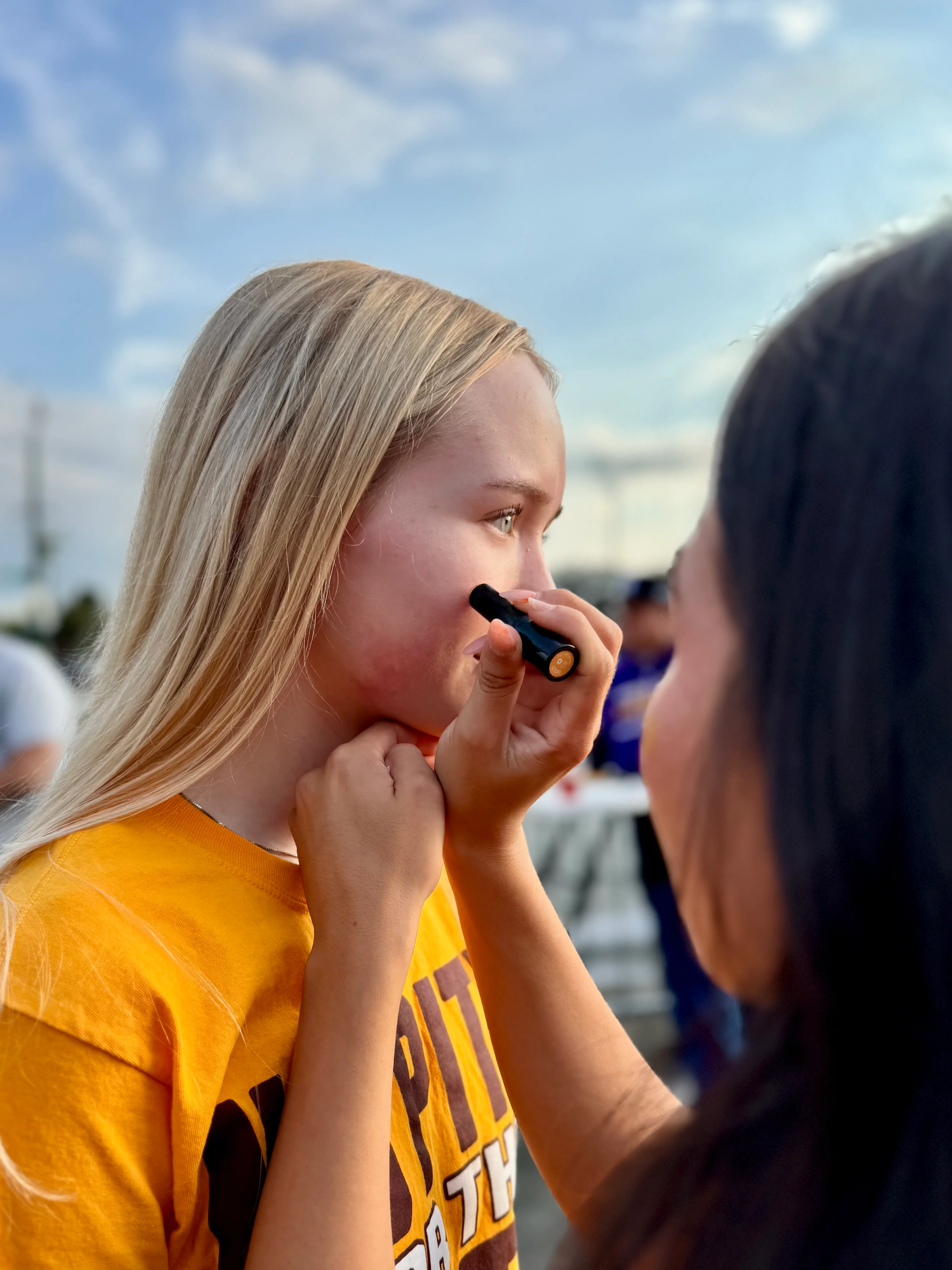 Two girls preparing for an event with face paint outdoors