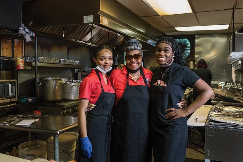 Three chefs smiling in a bustling restaurant kitchen