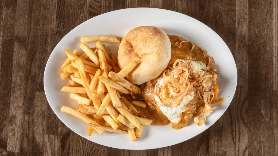 A plate of comfort food including fries, a bun, and a dish topped with a fried egg and crispy onions.