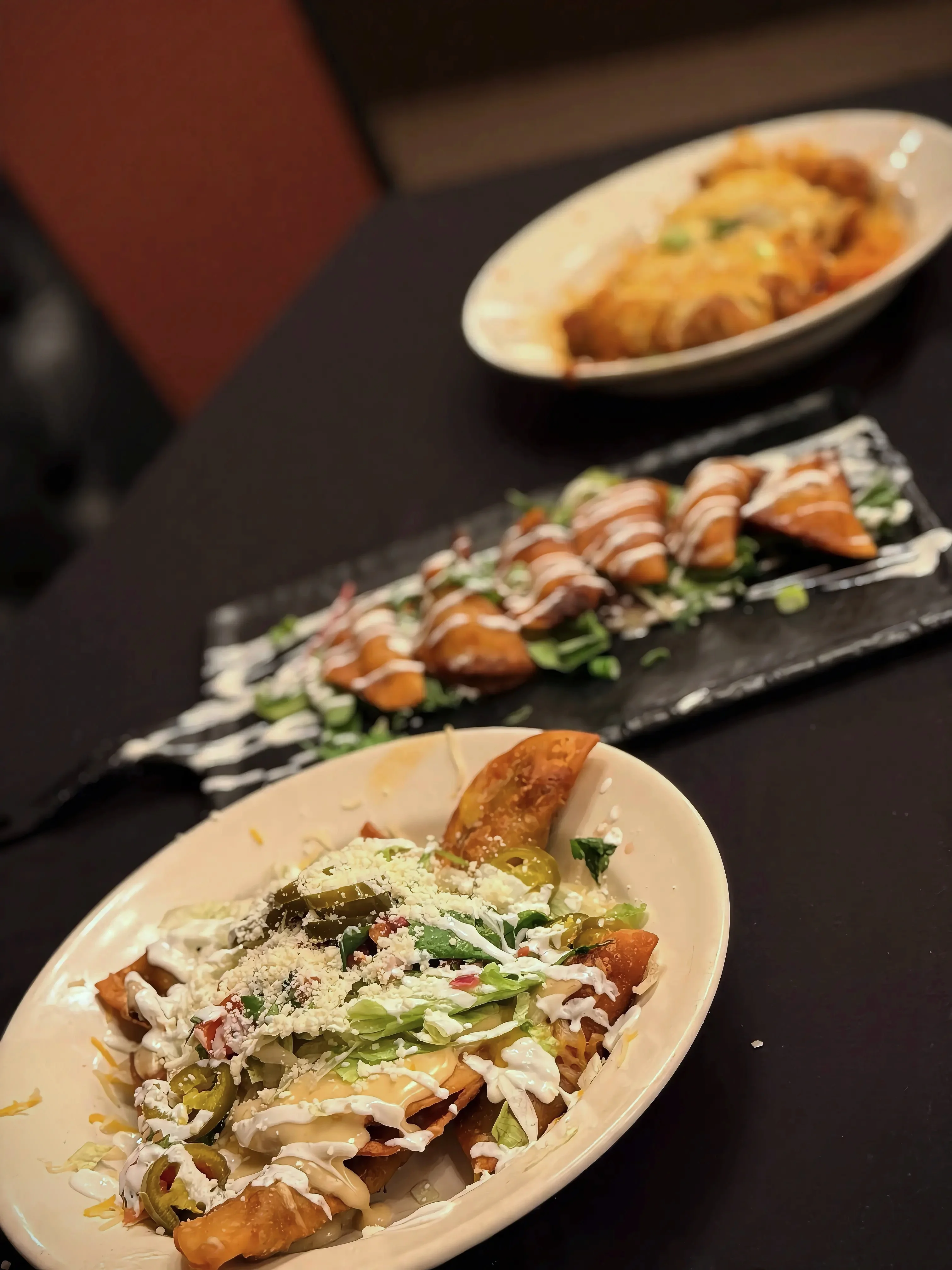 A serving of crispy tortilla chips topped with fresh lettuce, jalapeños, sour cream, and cheese, accompanied by other dishes in the background.