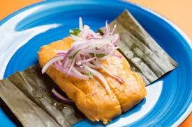 Peruvian tamal with onion garnish on banana leaves