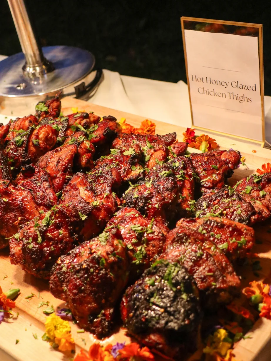 Hot honey glazed chicken thighs garnished with herbs on a wooden platter.