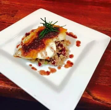 A beautifully plated dish of fish on a bed of grains, garnished with herbs and sauce.
