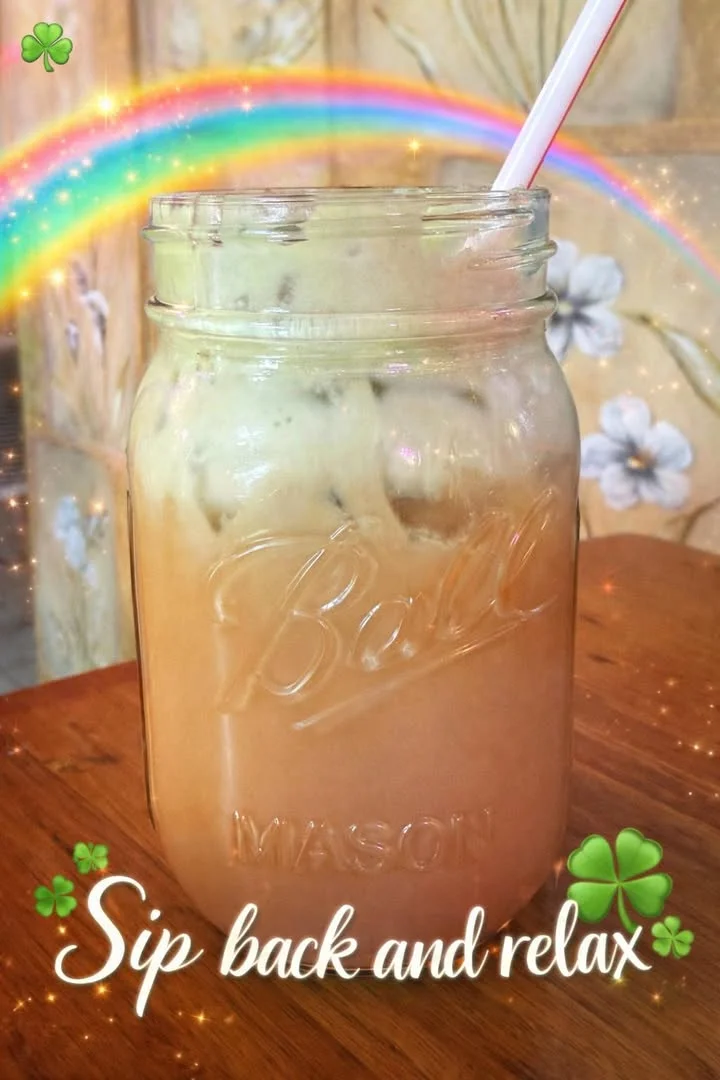 A mason jar filled with a creamy iced drink, complete with a straw. The background features a colorful rainbow and decorative elements.