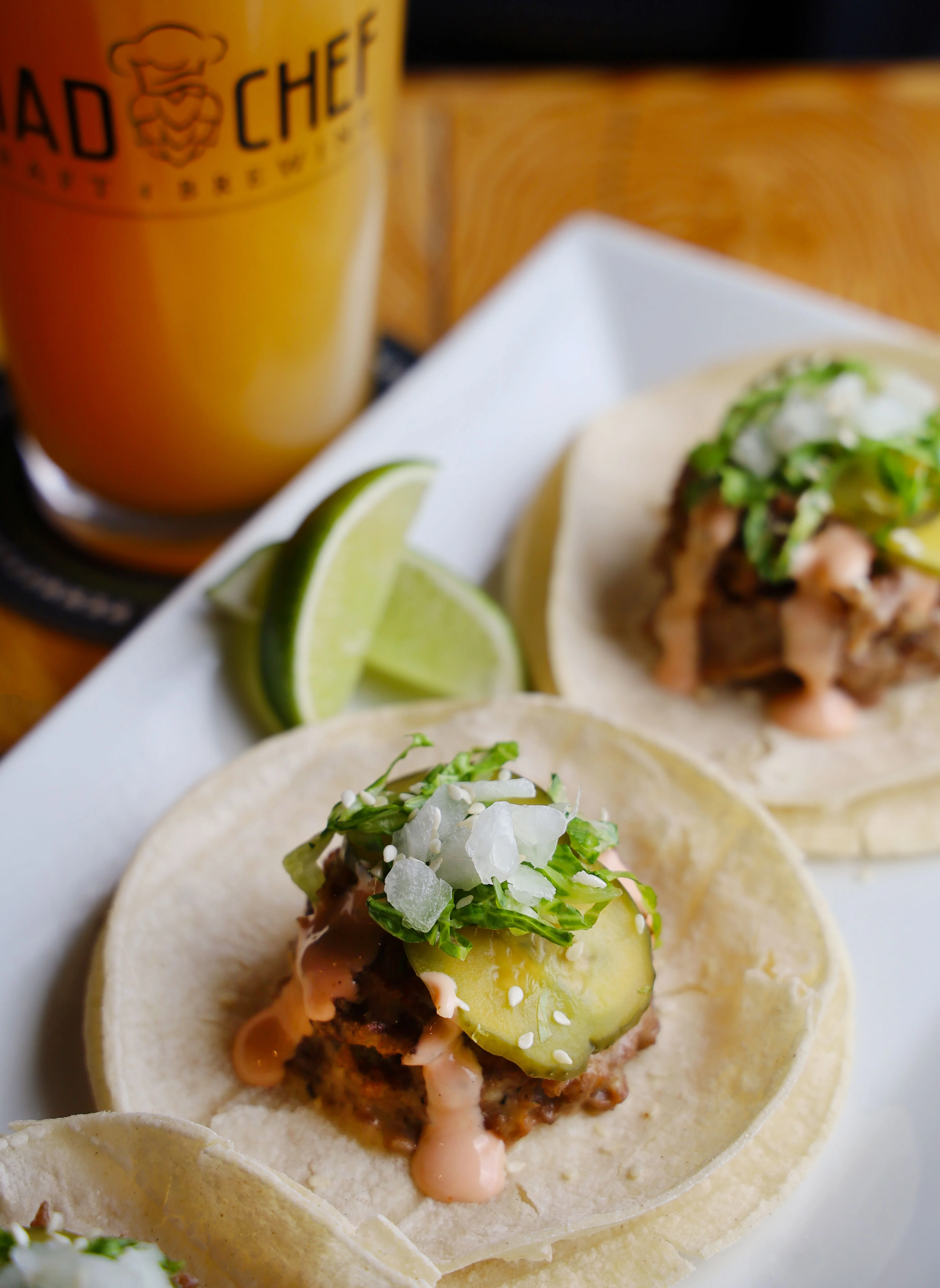 Three tacos with pulled meat, pineapple, and lime on a plate.