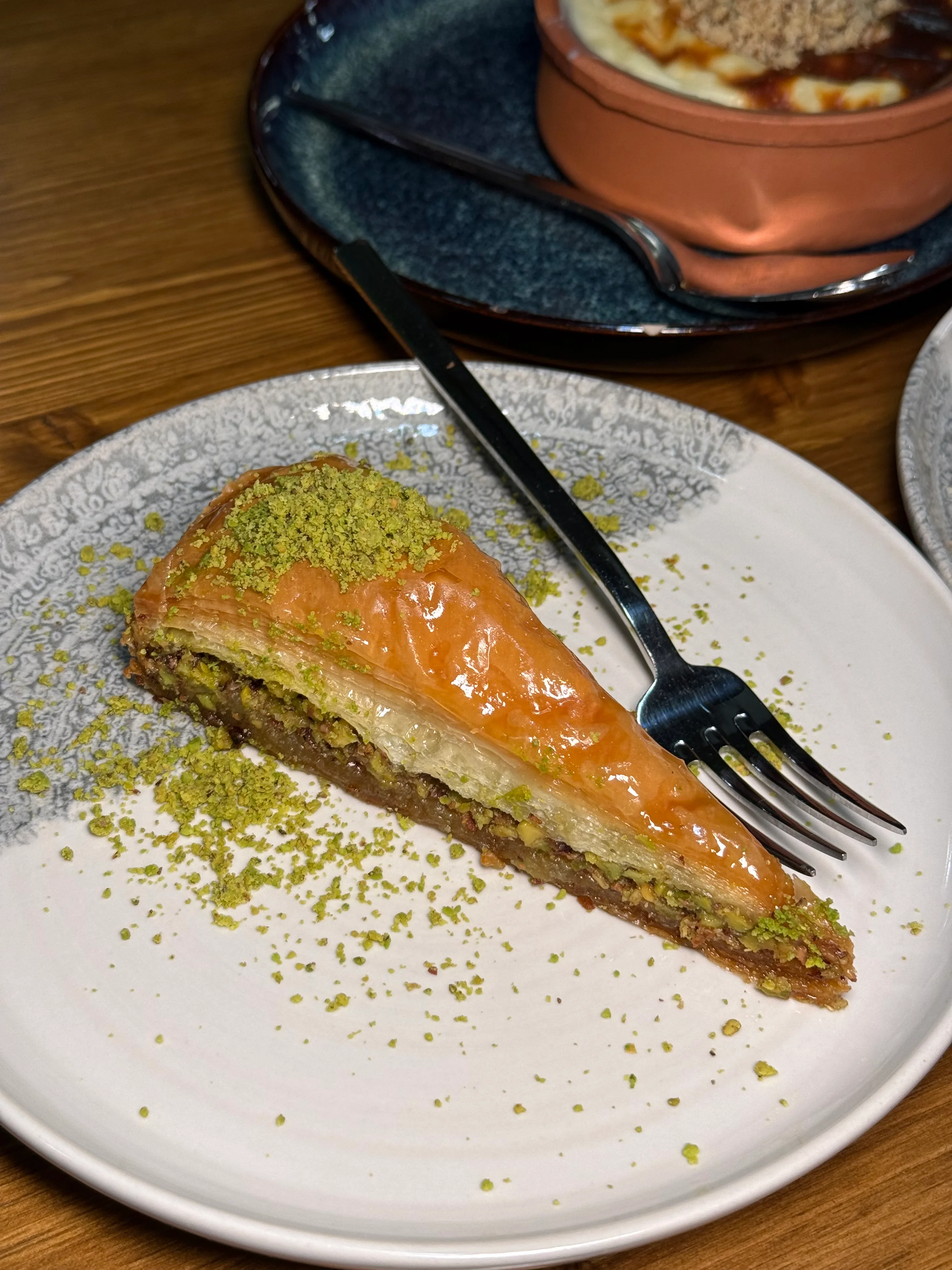 A close-up of a bowl of red pepper dip garnished with walnuts and cheese, drizzled with oil and sprinkled with herbs.