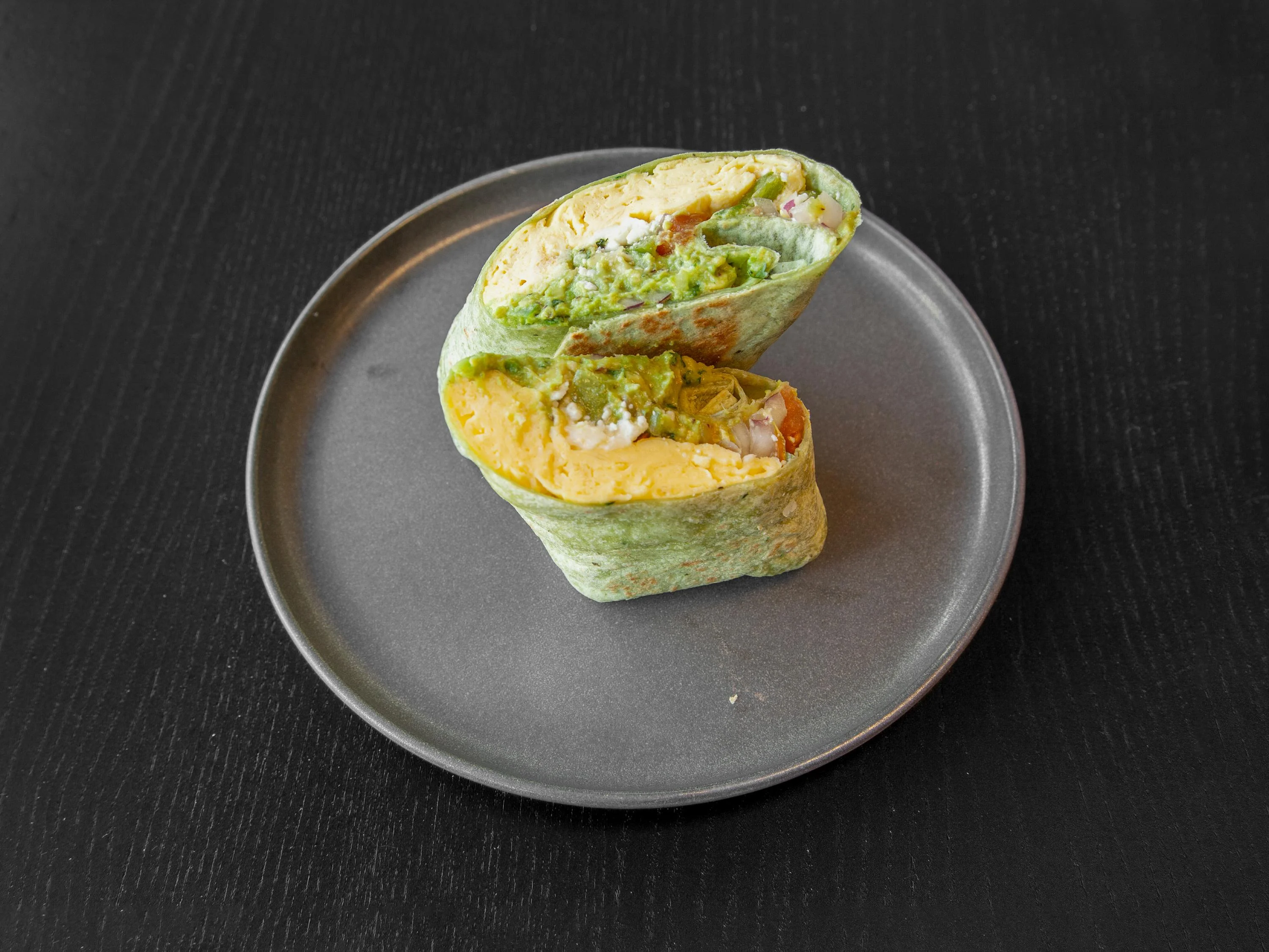 A spinach wrap filled with colorful ingredients, neatly cut in half and placed on a round plate.