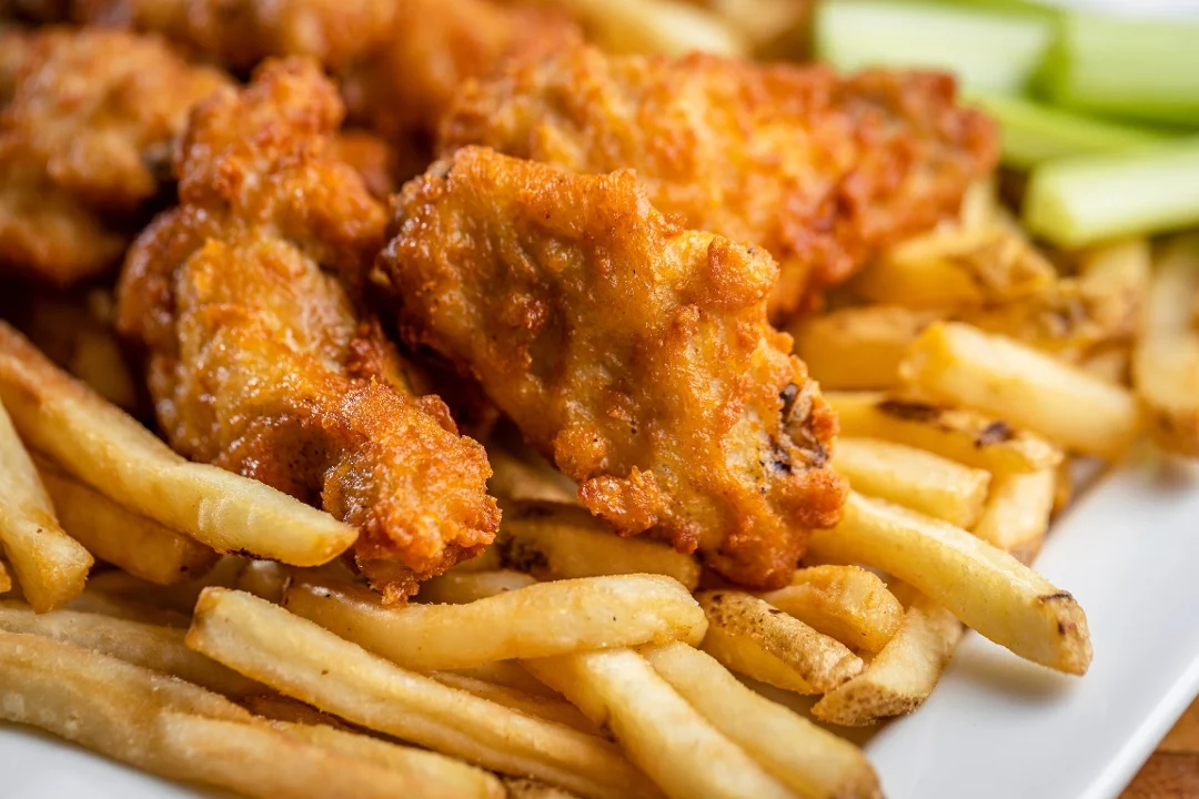 A delicious serving of fried chicken wings placed over a bed of crispy French fries, accompanied by slices of celery.