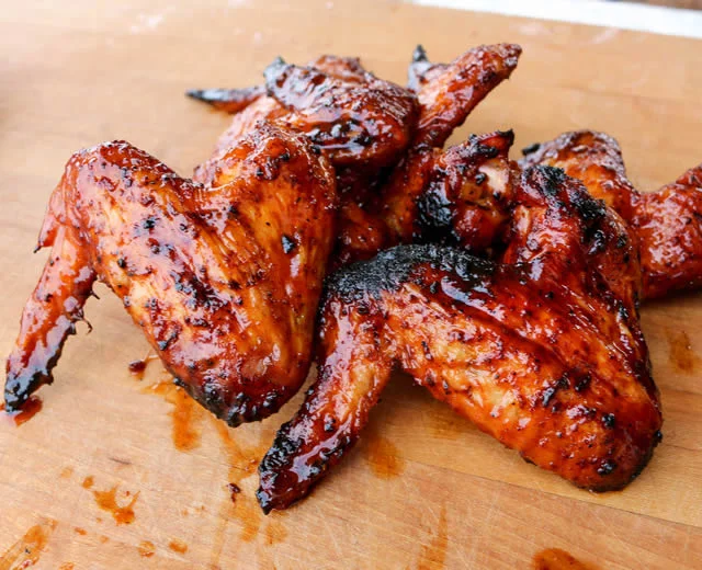 A pile of grilled chicken wings coated in a glossy barbecue sauce, arranged on a wooden surface.