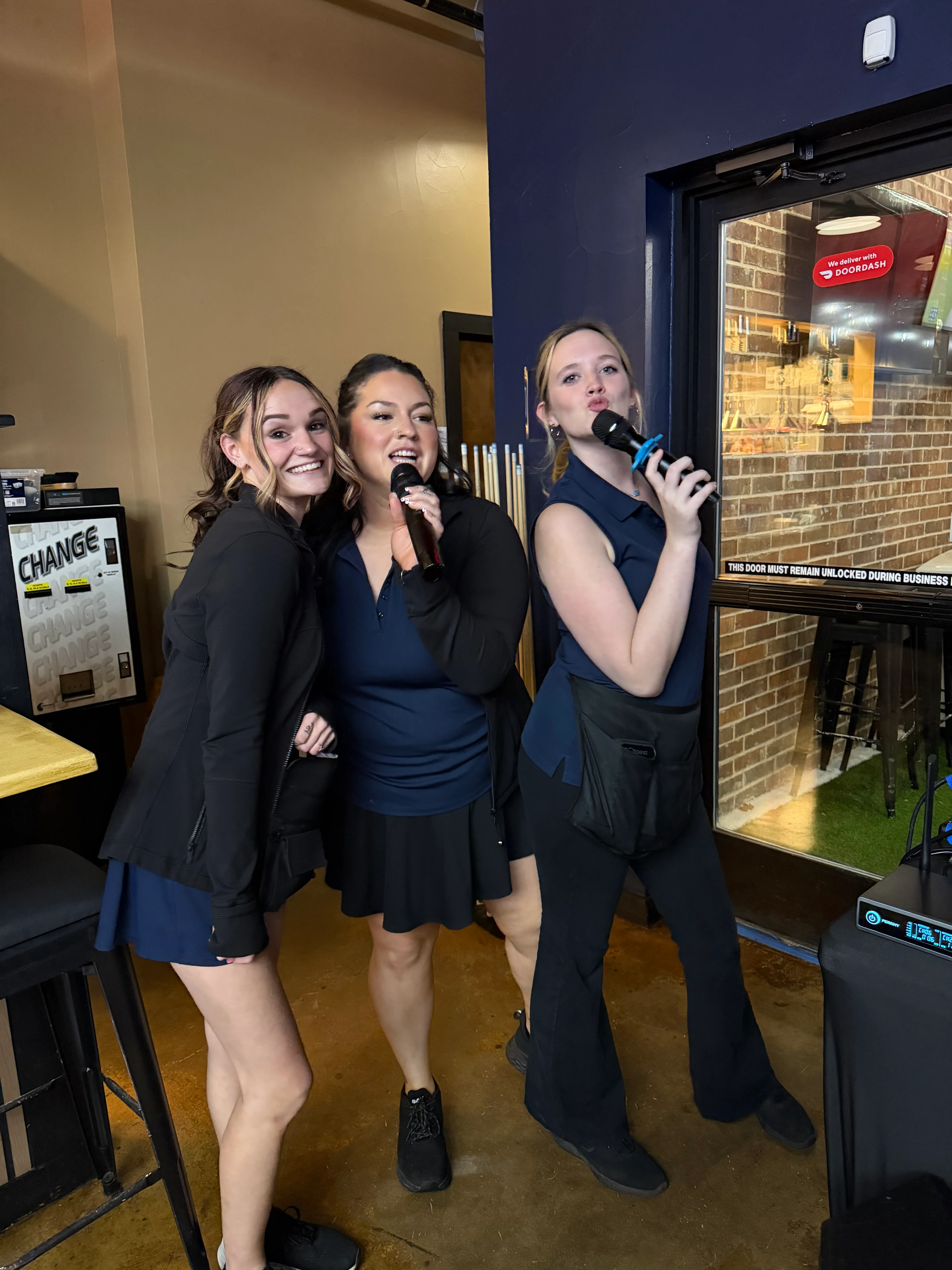 Three staff members singing with microphones in a lively restaurant setting