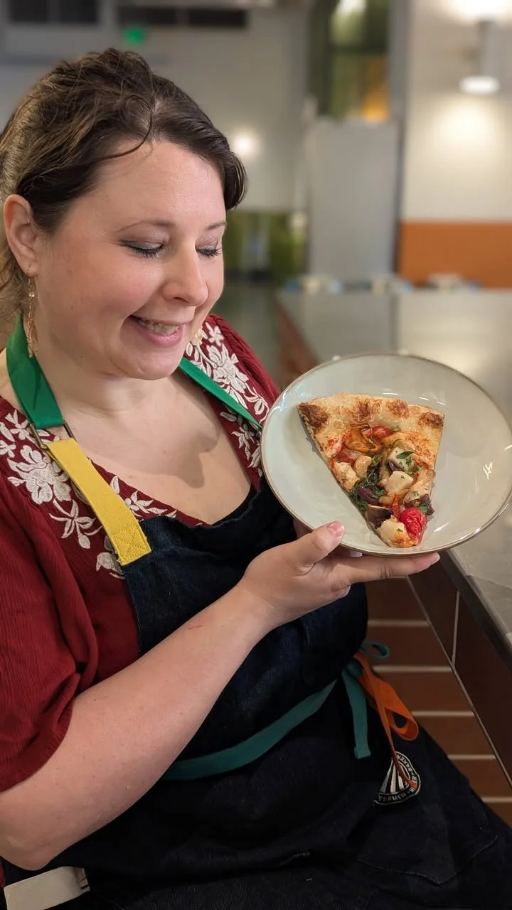 A person holding a plate with a slice of pizza topped with a variety of colorful vegetables and ingredients.